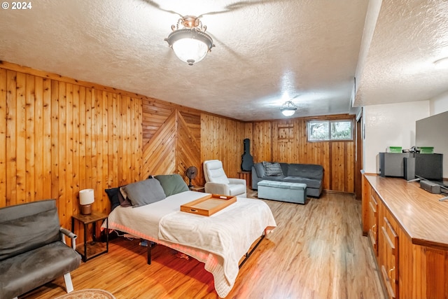 bedroom with wooden walls, light hardwood / wood-style floors, and a textured ceiling