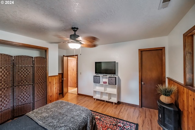 bedroom with a textured ceiling, ceiling fan, light hardwood / wood-style floors, a closet, and wood walls