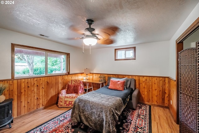 bedroom featuring ceiling fan, wood walls, a textured ceiling, and light hardwood / wood-style flooring