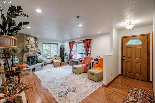 living room featuring a stone fireplace, a textured ceiling, and hardwood / wood-style flooring