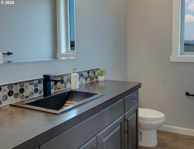 half bathroom with toilet, decorative backsplash, vanity, wood finished floors, and baseboards