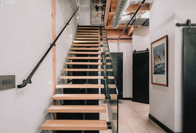 stairs featuring light hardwood / wood-style flooring, a towering ceiling, and a barn door