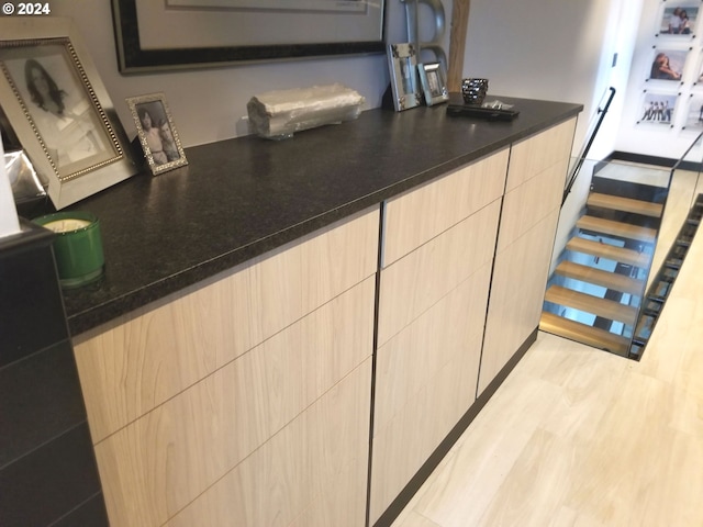 bar with light brown cabinetry, light hardwood / wood-style flooring, and dark stone countertops