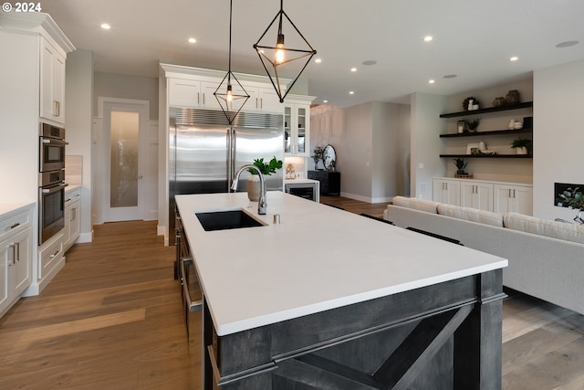 kitchen featuring stainless steel appliances, an island with sink, hardwood / wood-style flooring, white cabinets, and sink