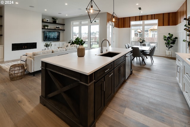 kitchen with sink, a fireplace, a kitchen island with sink, and light hardwood / wood-style flooring