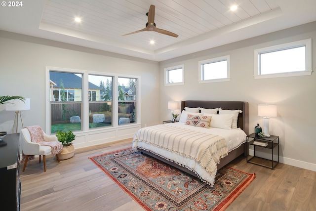 bedroom featuring ceiling fan, a raised ceiling, and light wood-type flooring