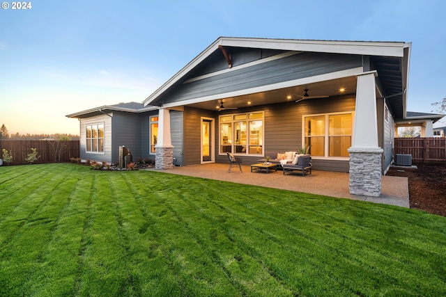 back house at dusk with ceiling fan, an outdoor living space, a patio, central AC, and a lawn