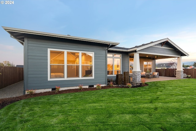 back house at dusk featuring a yard and a patio