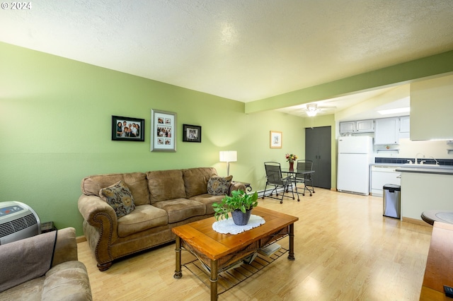 living area featuring ceiling fan, light wood-style floors, and a textured ceiling