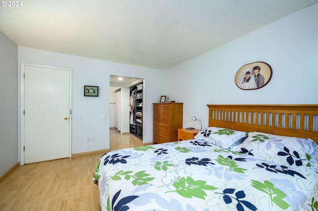 bedroom featuring a walk in closet, baseboards, and light wood-type flooring