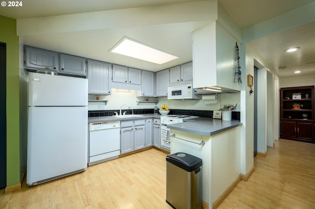 kitchen with dark countertops, gray cabinets, a sink, white appliances, and light wood-type flooring