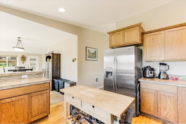 kitchen with stainless steel fridge with ice dispenser, light hardwood / wood-style flooring, and hanging light fixtures