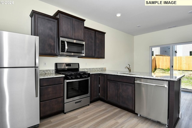 kitchen featuring sink, light hardwood / wood-style flooring, appliances with stainless steel finishes, light stone counters, and kitchen peninsula