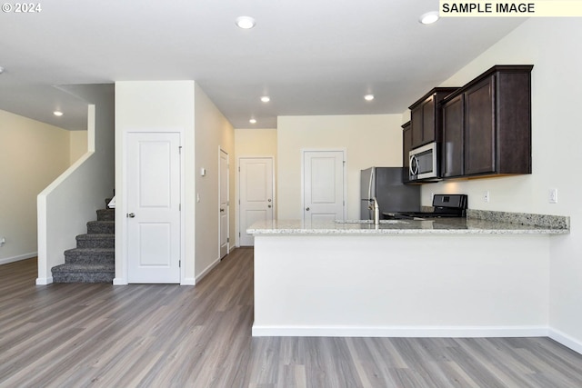 kitchen with light stone countertops, light wood-type flooring, stainless steel appliances, and kitchen peninsula