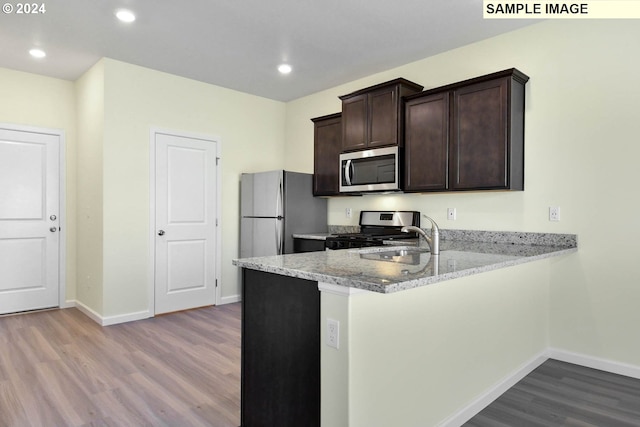 kitchen featuring kitchen peninsula, light stone countertops, light wood-type flooring, and stainless steel appliances