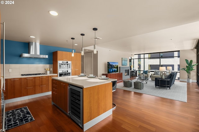 kitchen featuring a kitchen island, beverage cooler, stainless steel double oven, wood-type flooring, and wall chimney exhaust hood