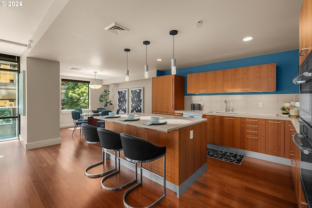 kitchen with hardwood / wood-style flooring, pendant lighting, decorative backsplash, sink, and a kitchen island