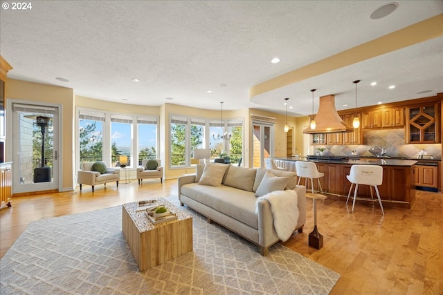 living room with a textured ceiling, sink, a notable chandelier, and light hardwood / wood-style flooring