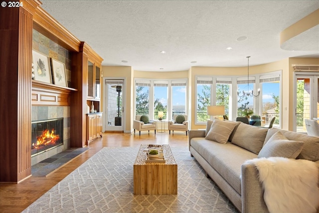 living room with hardwood / wood-style floors, a tile fireplace, a healthy amount of sunlight, and a notable chandelier