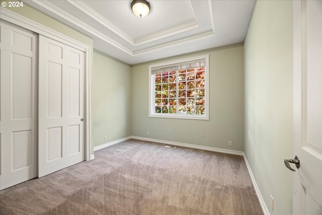 unfurnished bedroom with light colored carpet, a closet, crown molding, and a tray ceiling