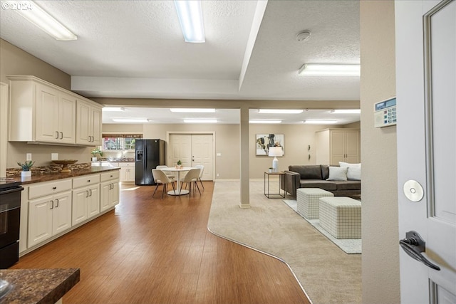 interior space featuring white cabinets, light hardwood / wood-style flooring, black refrigerator with ice dispenser, and a textured ceiling