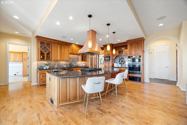 kitchen featuring pendant lighting, custom range hood, a large island with sink, and light hardwood / wood-style floors