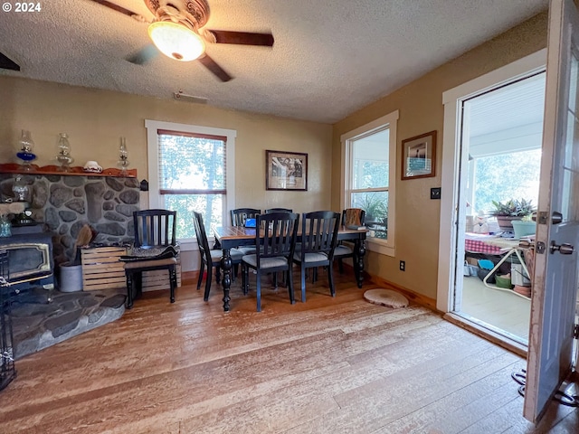 dining space with a ceiling fan, a wood stove, wood-type flooring, and a textured ceiling