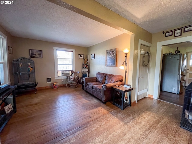 living area featuring a textured ceiling, cooling unit, wood finished floors, and baseboards