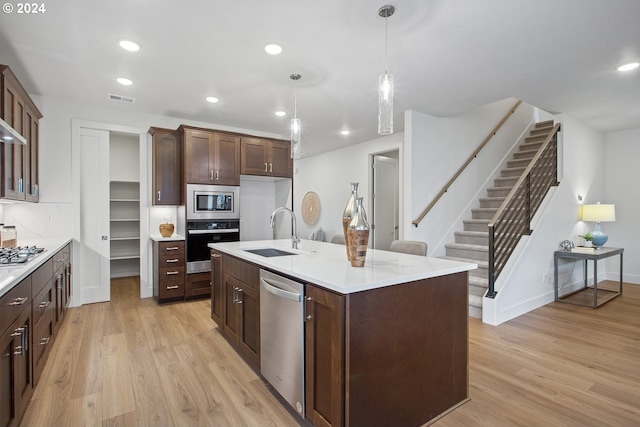 kitchen with light hardwood / wood-style floors, sink, a center island with sink, appliances with stainless steel finishes, and decorative light fixtures