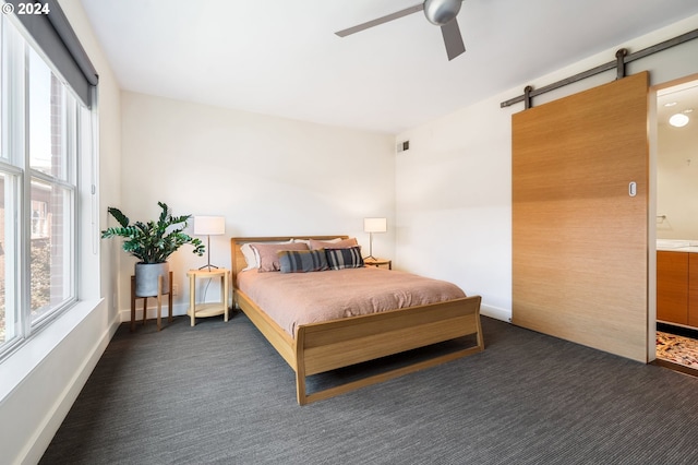 bedroom featuring multiple windows, baseboards, dark carpet, and a barn door