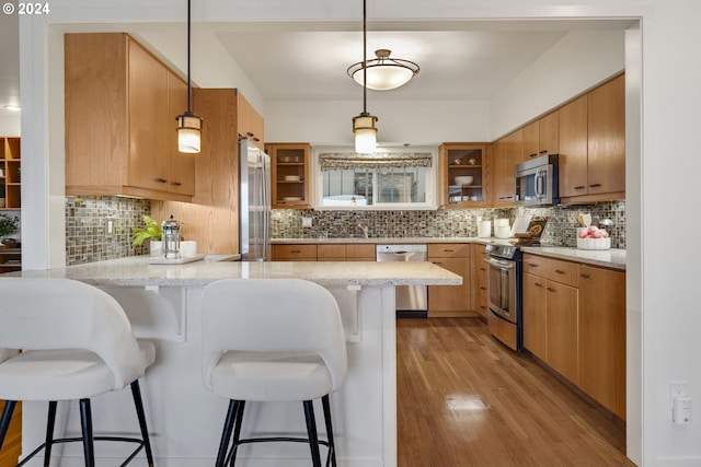 kitchen featuring kitchen peninsula, a kitchen bar, stainless steel appliances, decorative light fixtures, and light hardwood / wood-style flooring