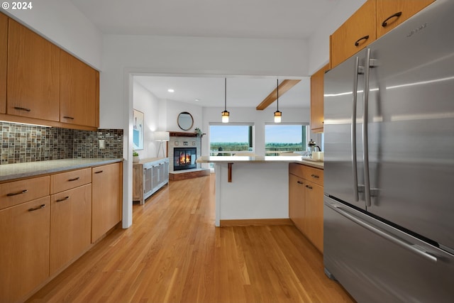 kitchen with tasteful backsplash, light hardwood / wood-style flooring, kitchen peninsula, stainless steel fridge, and decorative light fixtures