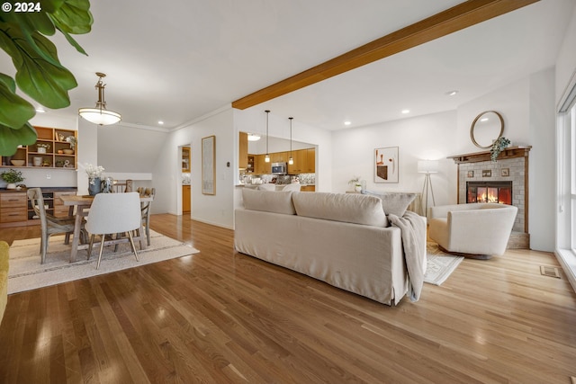 living room with beam ceiling, a tiled fireplace, crown molding, and hardwood / wood-style flooring