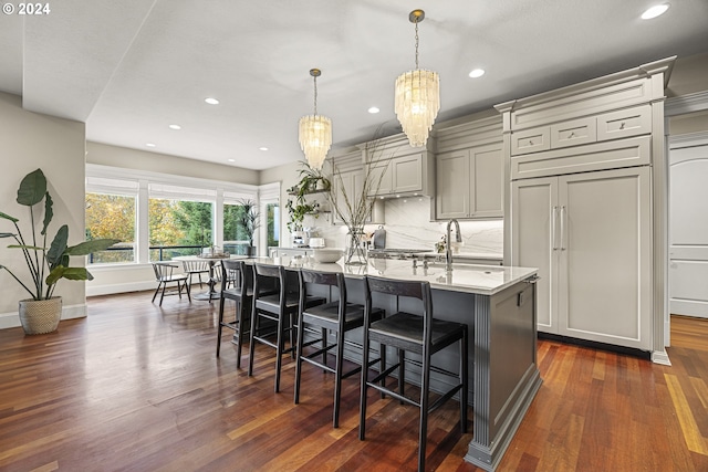 kitchen featuring decorative light fixtures, backsplash, an island with sink, dark wood-type flooring, and gray cabinetry