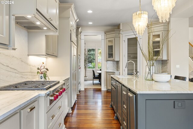 kitchen with dark hardwood / wood-style flooring, hanging light fixtures, decorative backsplash, sink, and an island with sink