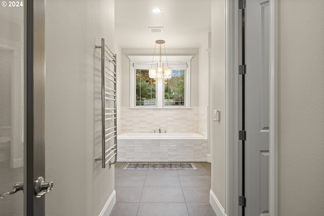 bathroom with tiled bath, tile patterned flooring, and an inviting chandelier