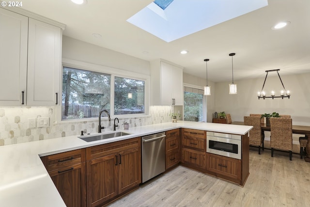 kitchen with a skylight, sink, light hardwood / wood-style flooring, pendant lighting, and appliances with stainless steel finishes