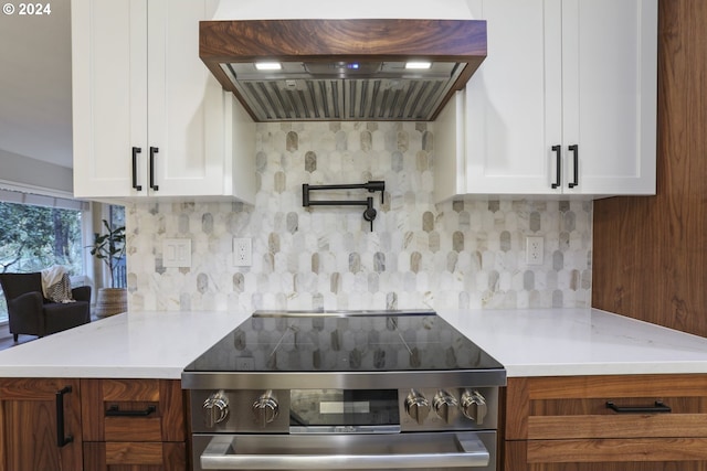 kitchen featuring decorative backsplash, light stone counters, custom range hood, stainless steel electric stove, and white cabinetry