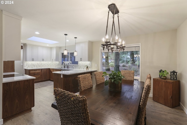 dining room with a skylight, sink, light hardwood / wood-style floors, and a notable chandelier