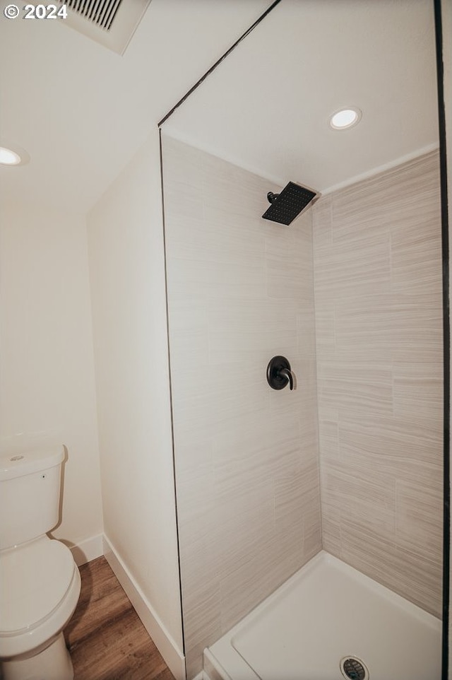 bathroom with tiled shower, hardwood / wood-style flooring, and toilet