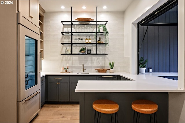 bar featuring gray cabinets, light hardwood / wood-style floors, tasteful backsplash, sink, and built in refrigerator