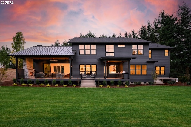 back house at dusk featuring a lawn, ceiling fan, and covered porch