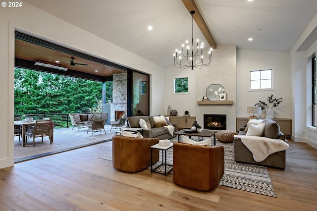 living room with ceiling fan with notable chandelier, vaulted ceiling with beams, a fireplace, and light hardwood / wood-style floors