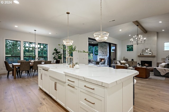 kitchen featuring hanging light fixtures, a kitchen island with sink, a large fireplace, and light hardwood / wood-style flooring