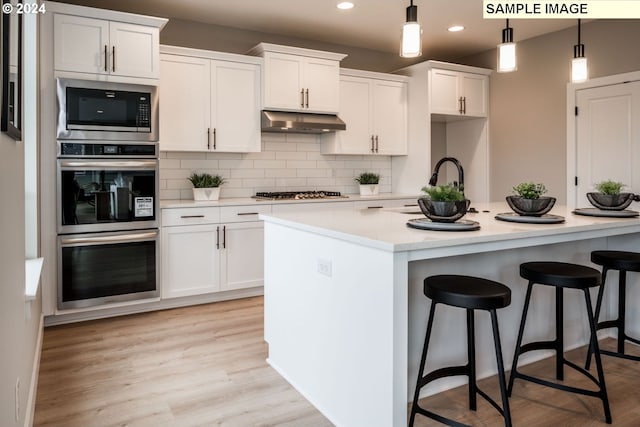 kitchen featuring backsplash, decorative light fixtures, a kitchen island with sink, white cabinets, and appliances with stainless steel finishes