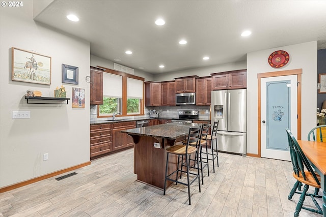 kitchen with a center island, stainless steel appliances, light hardwood / wood-style floors, sink, and dark stone counters