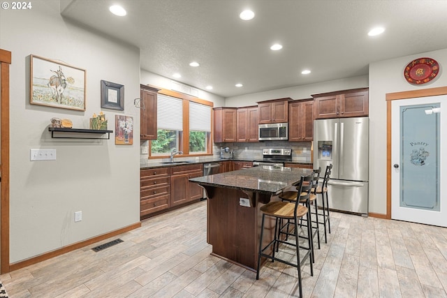 kitchen with stainless steel appliances, light hardwood / wood-style floors, a kitchen island, tasteful backsplash, and a breakfast bar