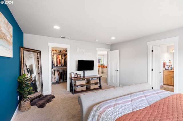 bedroom featuring a spacious closet, a closet, ensuite bathroom, and light colored carpet