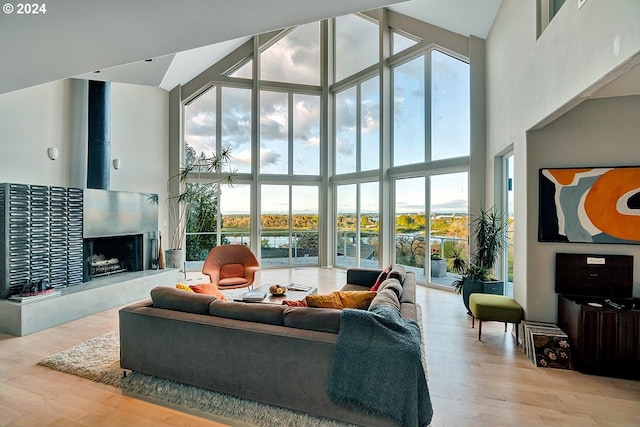 living room featuring a fireplace with raised hearth, wood finished floors, a towering ceiling, and floor to ceiling windows