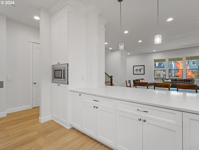 kitchen featuring kitchen peninsula, hanging light fixtures, white cabinets, light hardwood / wood-style floors, and stainless steel microwave